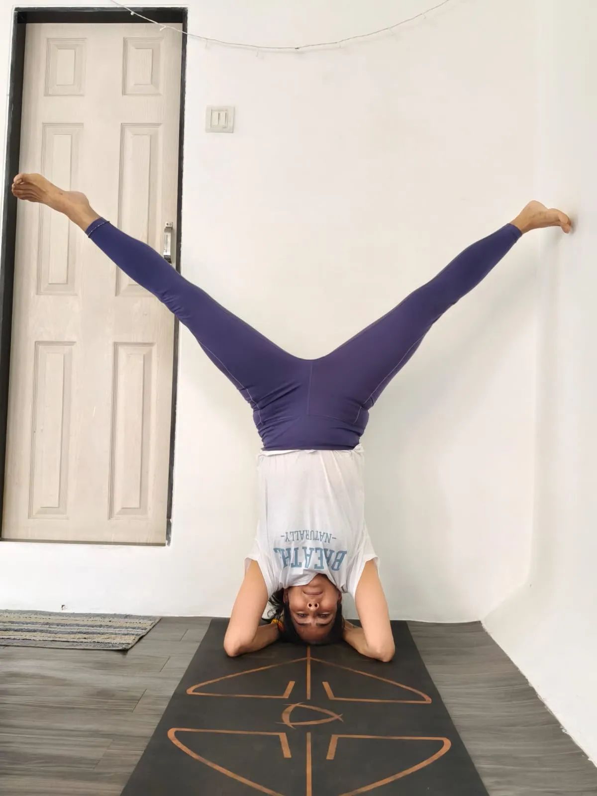 Headstand with legs opened wide against a white wall