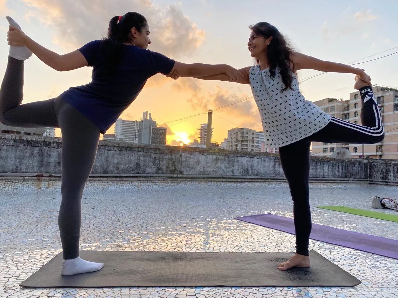 Two women in partner dancer’s pose on a rooftop at sunset